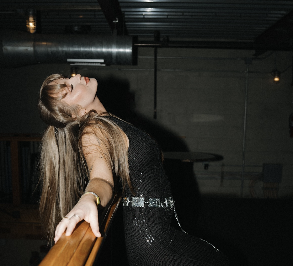 Ashley standing by a railing posing in a black dress.